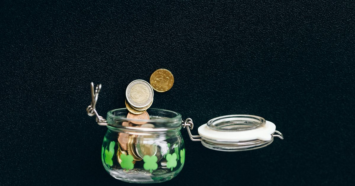 Three clear glass jars in a row with hand-decorated labels reading Save, Spend, and Share, sitting on a wooden kitchen counter.